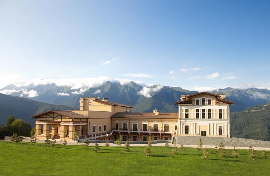 The classic yellow façade of Solis Sochi Hotel set against the green mountains of the Caucasus in summer