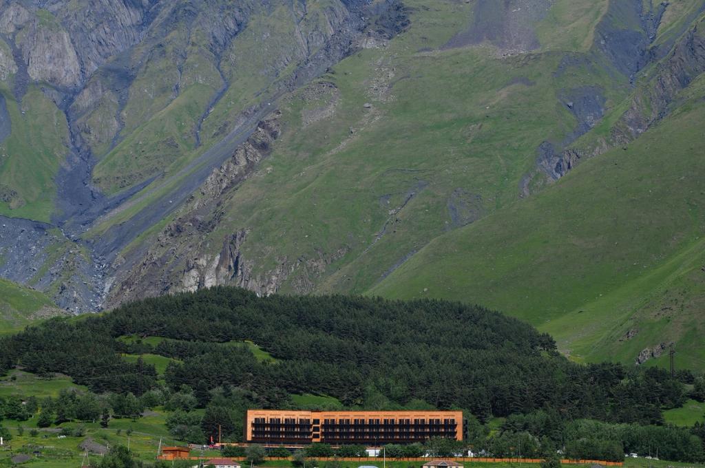 The Rooms Kazbegi hotel building at the foot of a verdant Caucasian mountainside
