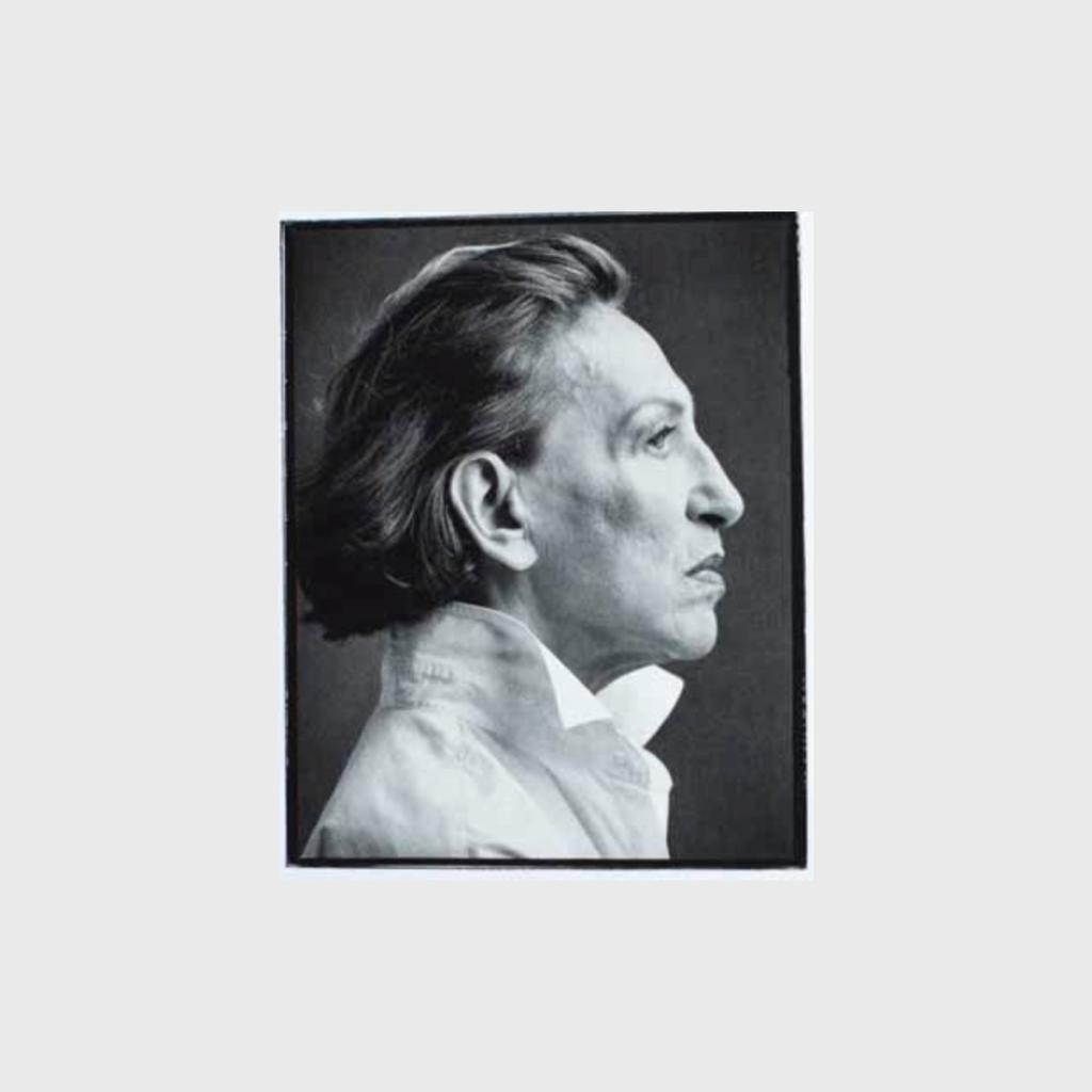 A black-and-white profile portrait of a man with slicked-back hair in a white shirt