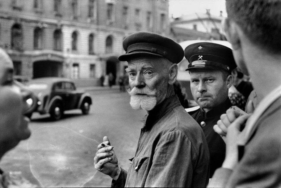 An elderly man with grey moustache and a cigarette, among the crowd on a Moscow street