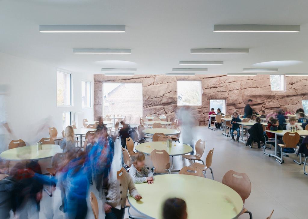 The canteen of The Roc School with round tables and a pink stone wall punctuated by windows