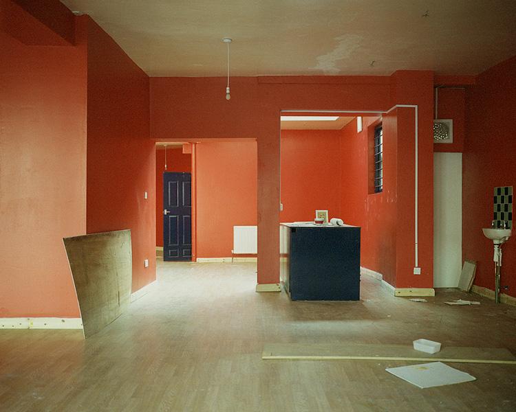 An empty room with bright orange walls in the middle of renovation, building materials scattered across the floor