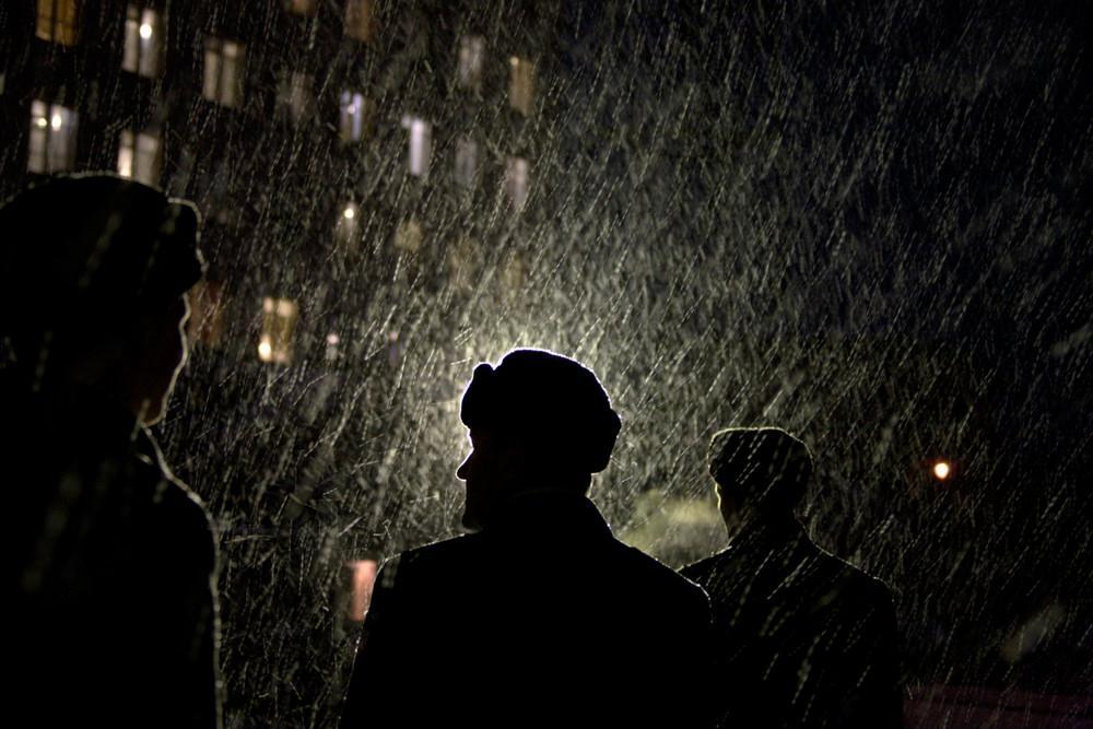 Silhouettes of people in hats against the lit windows of a building through heavy snowfall