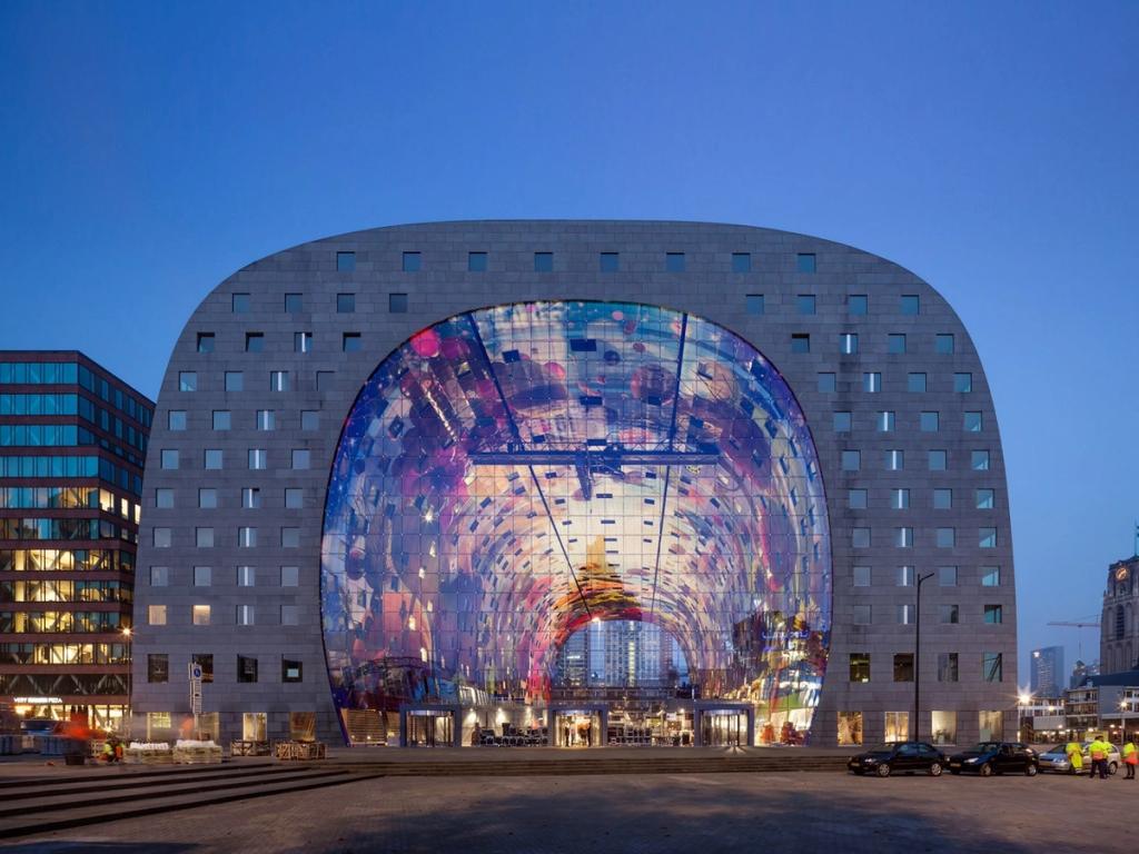 The horseshoe-shaped facade of Rotterdam's Markthal, with its colourful fresco beneath the arch, at evening
