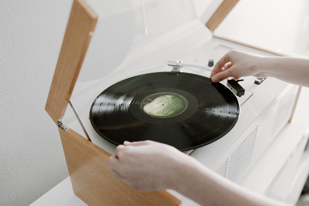 Hands place a black vinyl record onto the Braun SK55 turntable