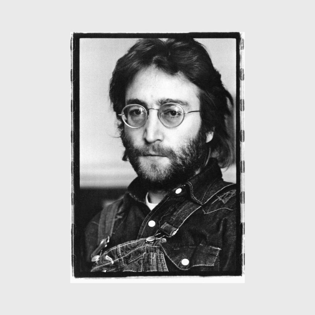 A black-and-white portrait of John Lennon wearing a denim jacket and round glasses, with a beard