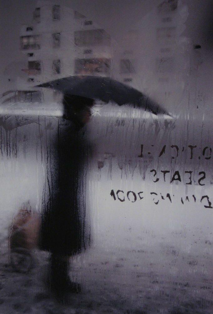 The silhouette of a figure holding an umbrella, seen through a rain-streaked, misted window pane
