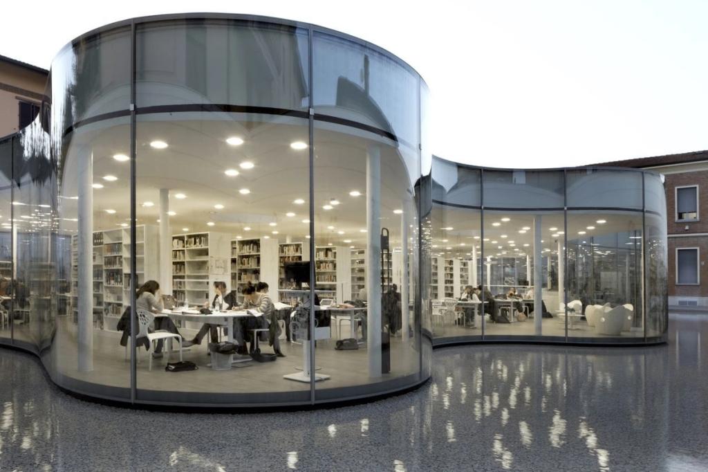 The MABIC Library at night, its curved glass volume illuminated with readers seated at tables inside
