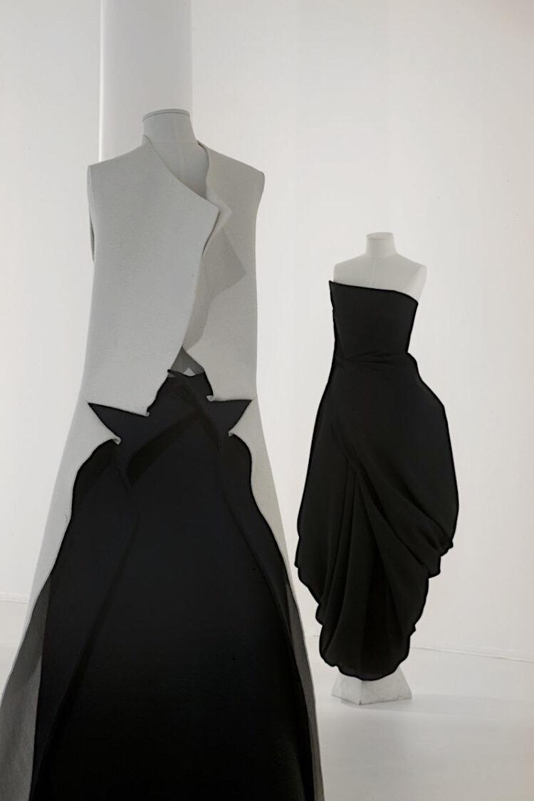Two mannequins in asymmetric black-and-white draped dresses in a bright gallery space
