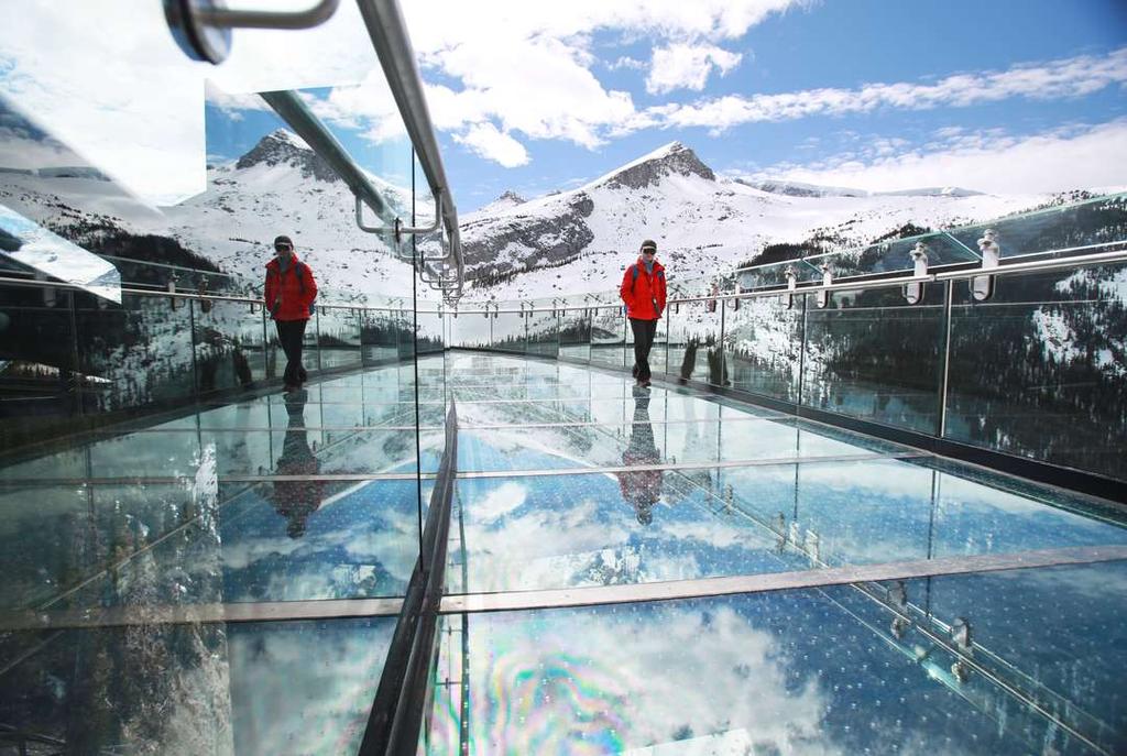 The Glacier Skywalk observation deck in Canada, with its glass floor and visitors set against a backdrop of snow-capped mountains