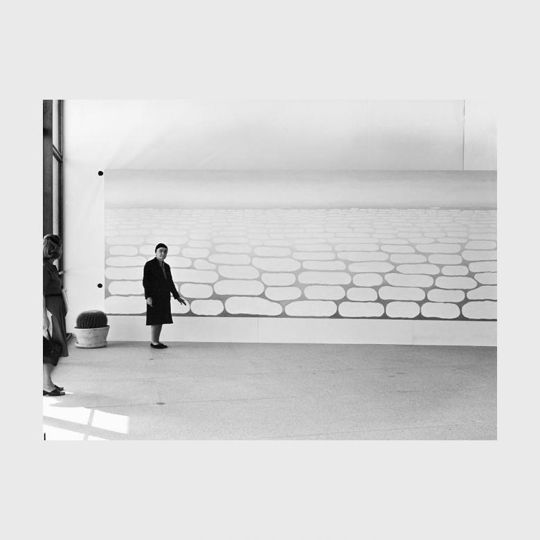 Black-and-white photograph: O'Keeffe in a gallery in front of a large canvas depicting clouds