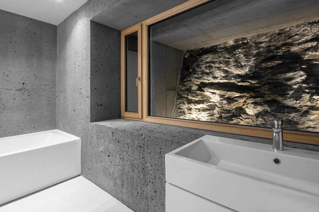 A bathroom with concrete walls and a window looking out onto bare rock