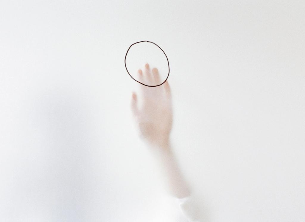 Work by Ina Jang: a pale female hand reaches towards a drawn circle on a white background
