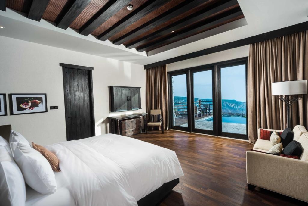 A bedroom with a wooden ceiling and glass doors opening onto a terrace with a pool above the gorge