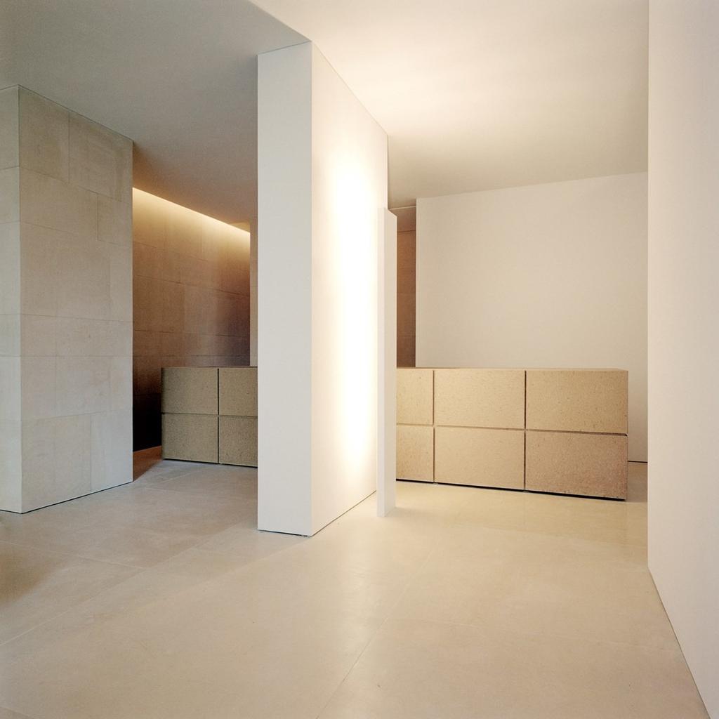 A minimalist entrance hall with a white column, limestone panels and low stone chests