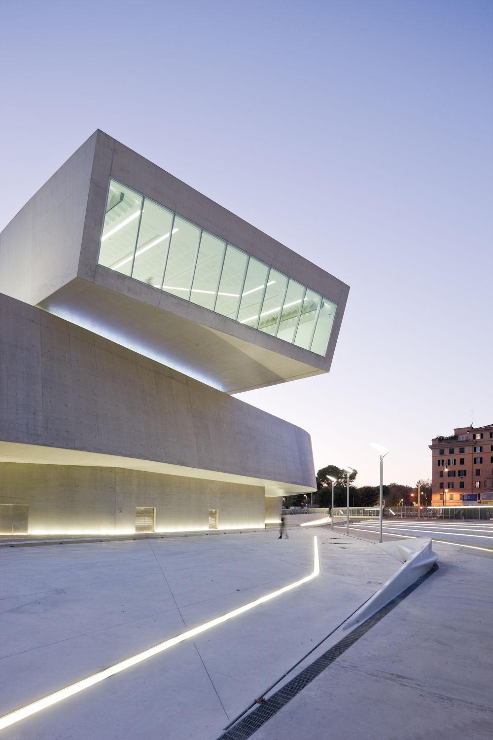 Бетонный консольный объём музея MAXXI со светящейся остеклённой галереей в сумерках