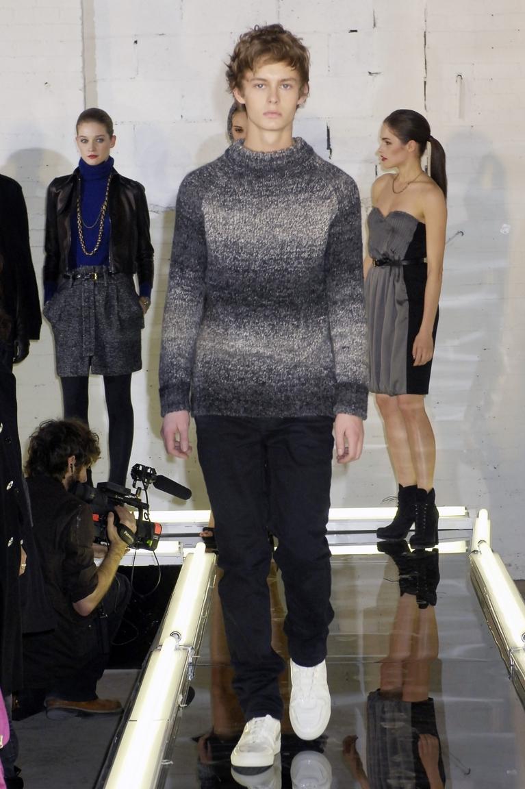 A menswear look from Alexander Wang featuring a grey marl sweater and dark trousers on the runway