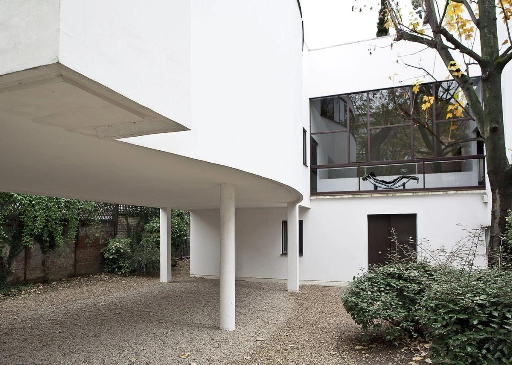 The white curved façade of Villa La Roche on pilotis, with a glazed gallery and garden