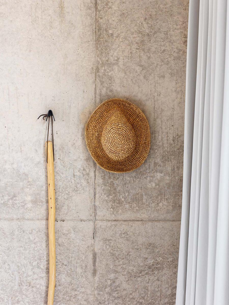 A straw hat and wooden cane hanging on a hook against a concrete wall in an Amangiri room