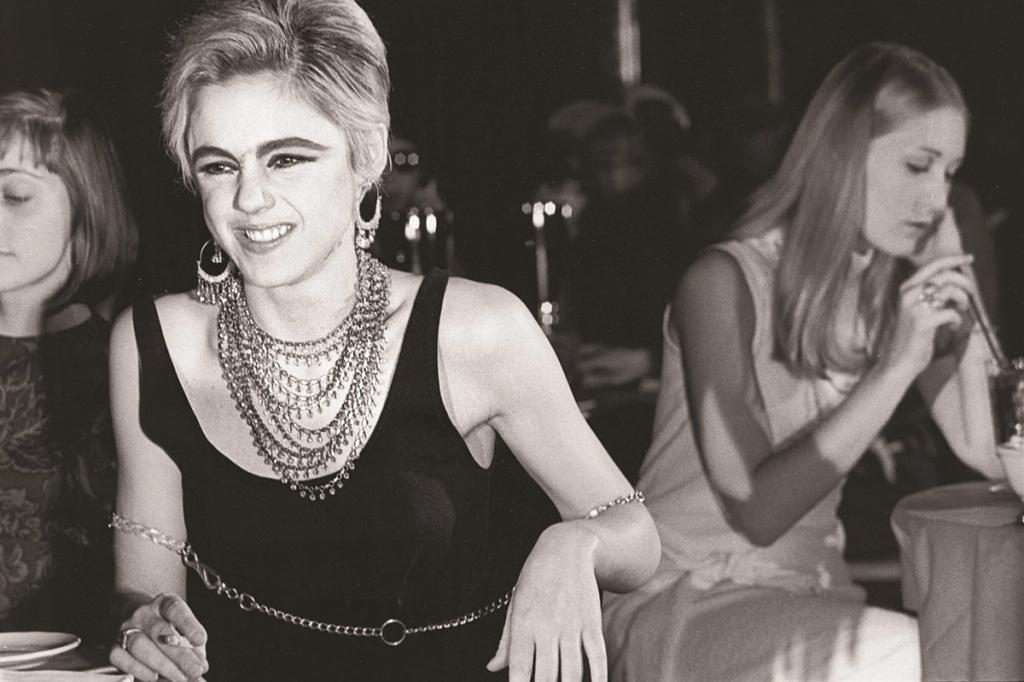 Black-and-white photograph of a smiling woman in a black dress and a chunky necklace at a nightclub