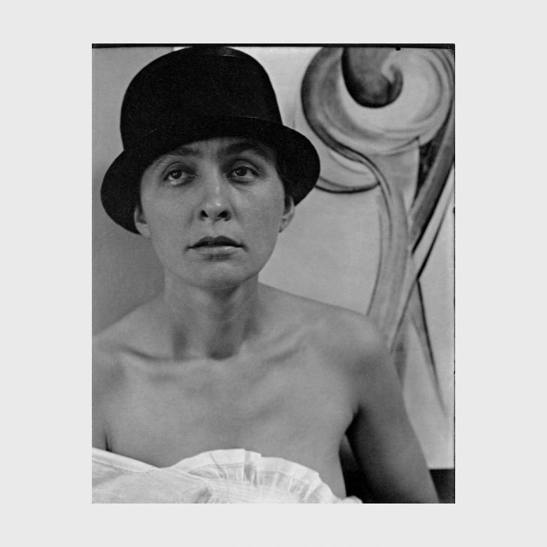 A Stieglitz black-and-white portrait: O'Keeffe in a black hat with bare shoulders