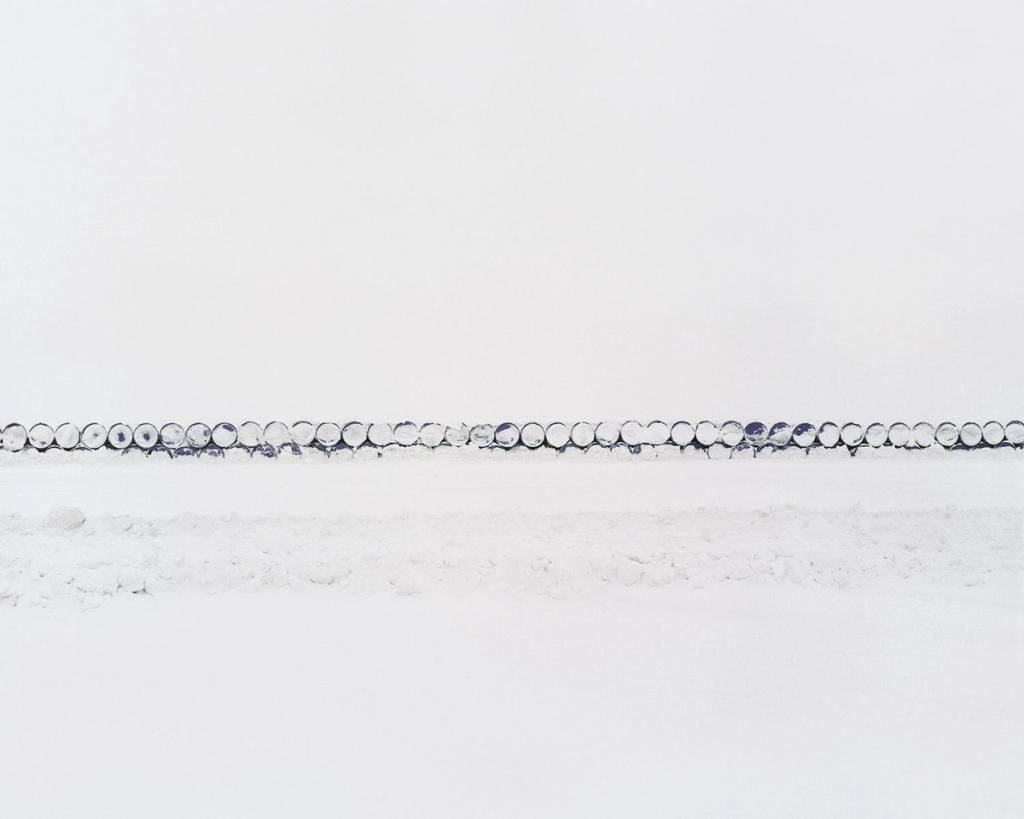 A long row of metal drums arranged in a line across a snowy field