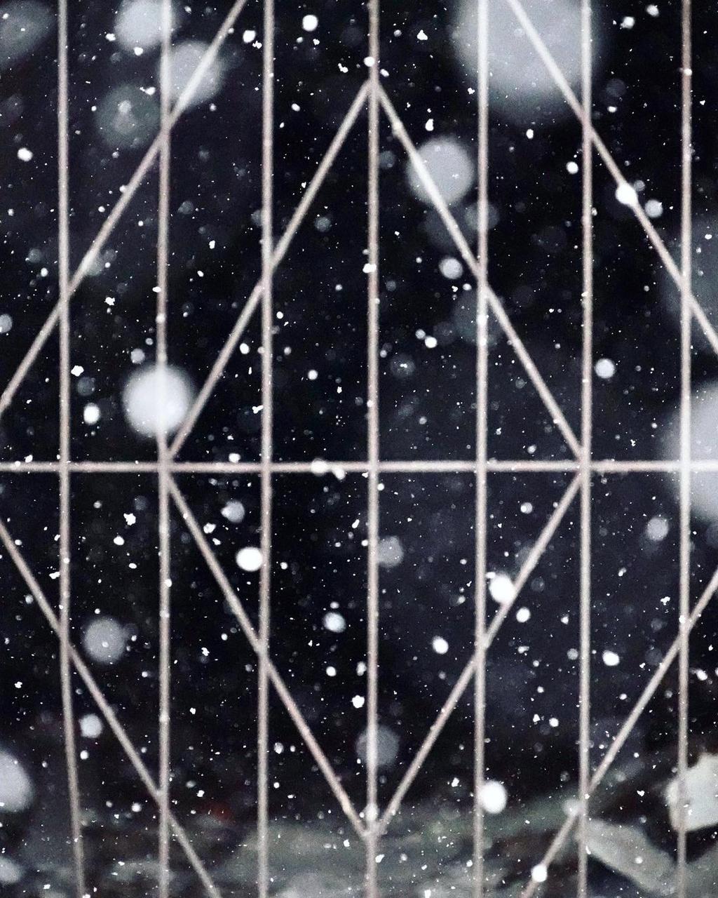 A diamond-patterned metal grille against falling snow at night