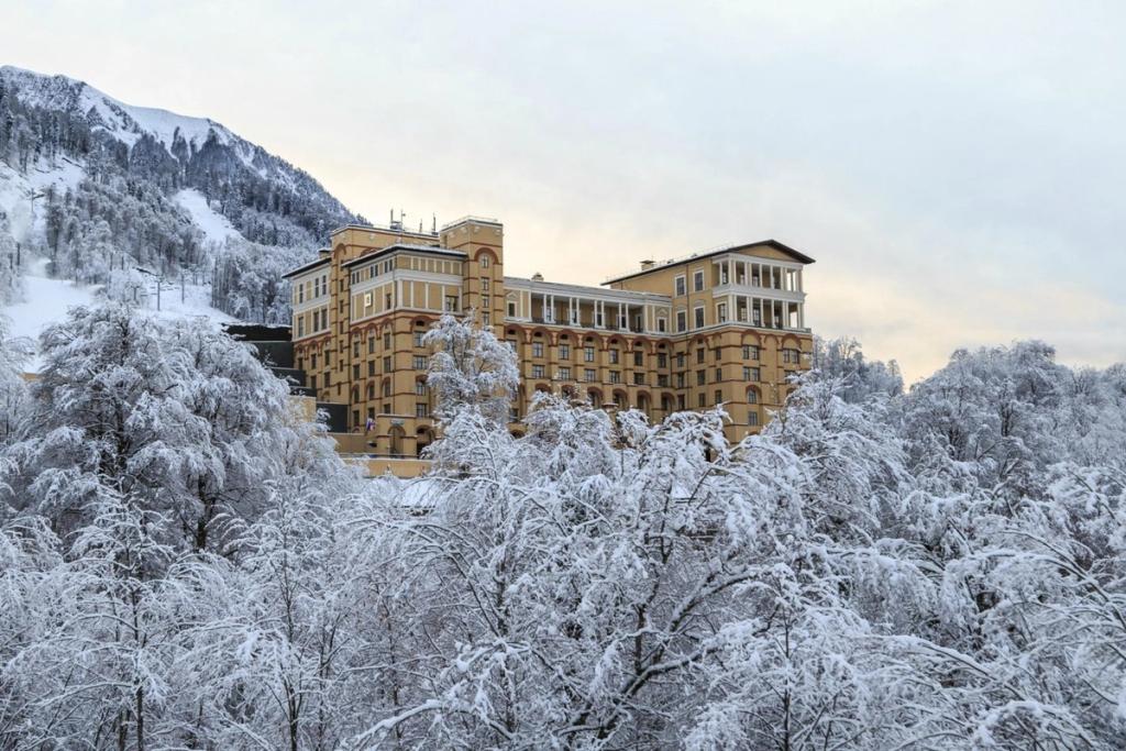 The yellow wing of Solis Sochi Hotel in winter, surrounded by the snow-covered forests of Krasnaya Polyana
