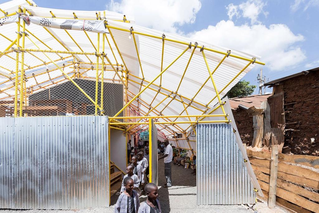 Kibera School: a yellow steel frame with a semi-transparent roof and corrugated metal walls; children gathered at the entrance