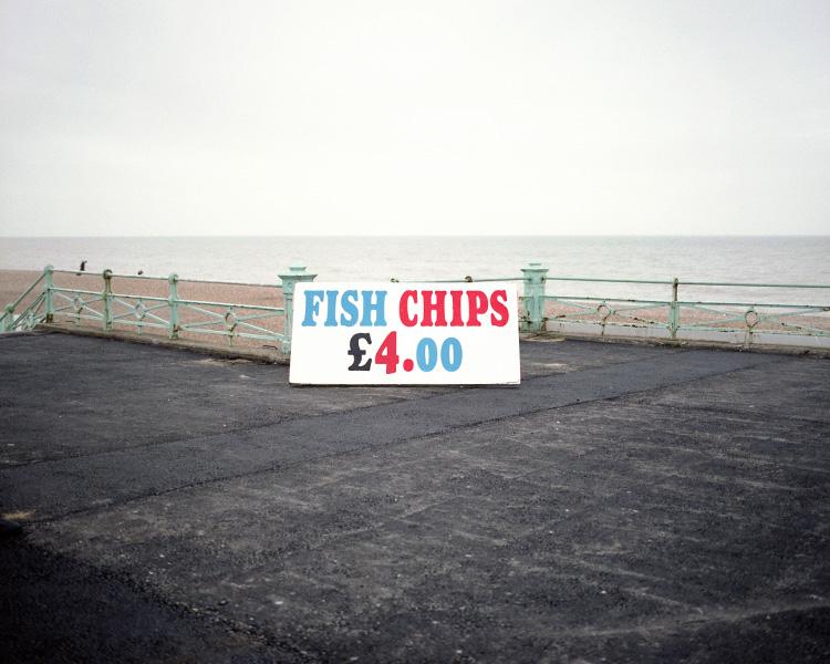 A Fish & Chips sign for four pounds on an empty embankment by a grey sea