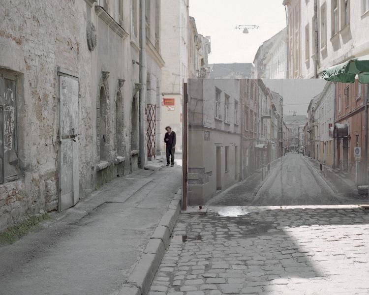 A person on a cobbled old street beside a large mirror reflecting another city street