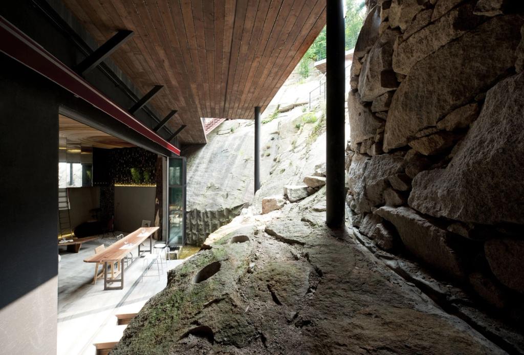 A wooden ceiling of a house cantilevering over a natural rock outcrop in the inner courtyard