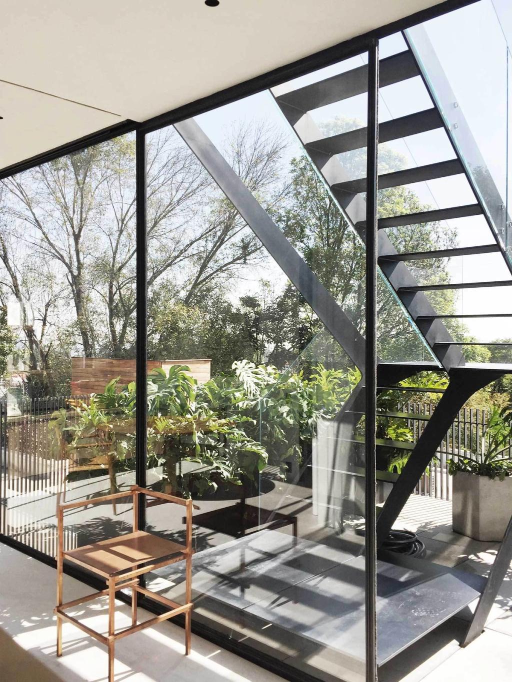 A steel staircase and glass walls looking out onto the tropical planting of a courtyard