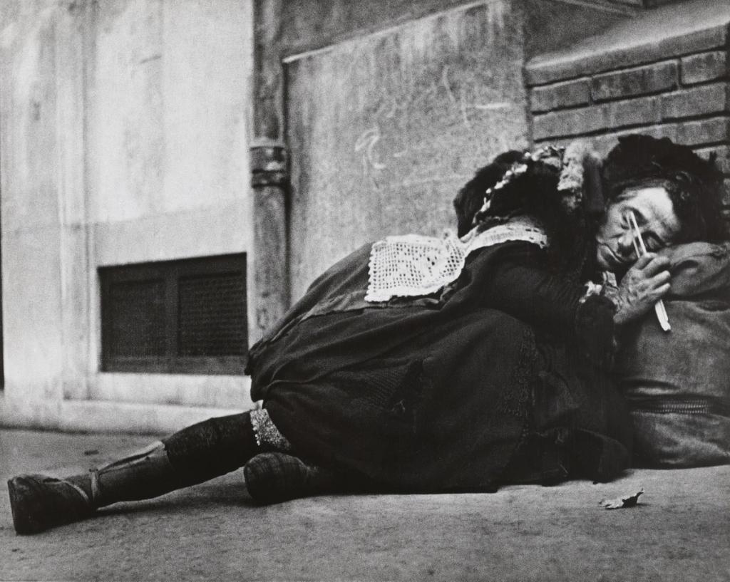 Бездомный человек в лохмотьях лежит на земле у стены с сигаретой