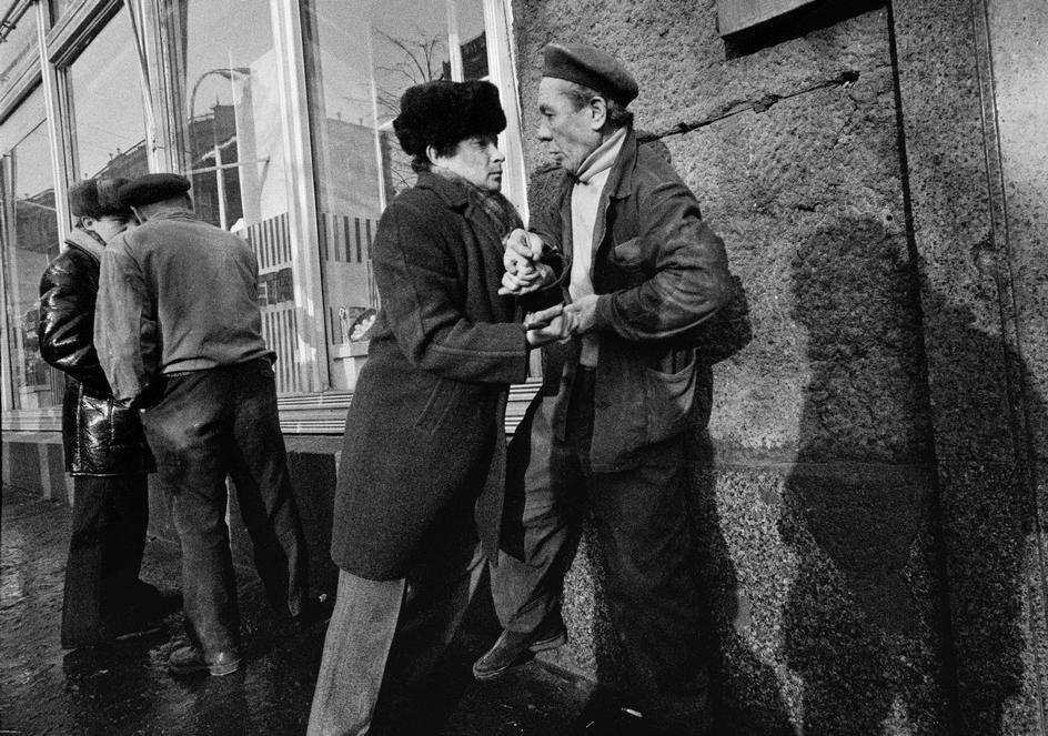 Two men in winter coats talking by a shop window on a street corner