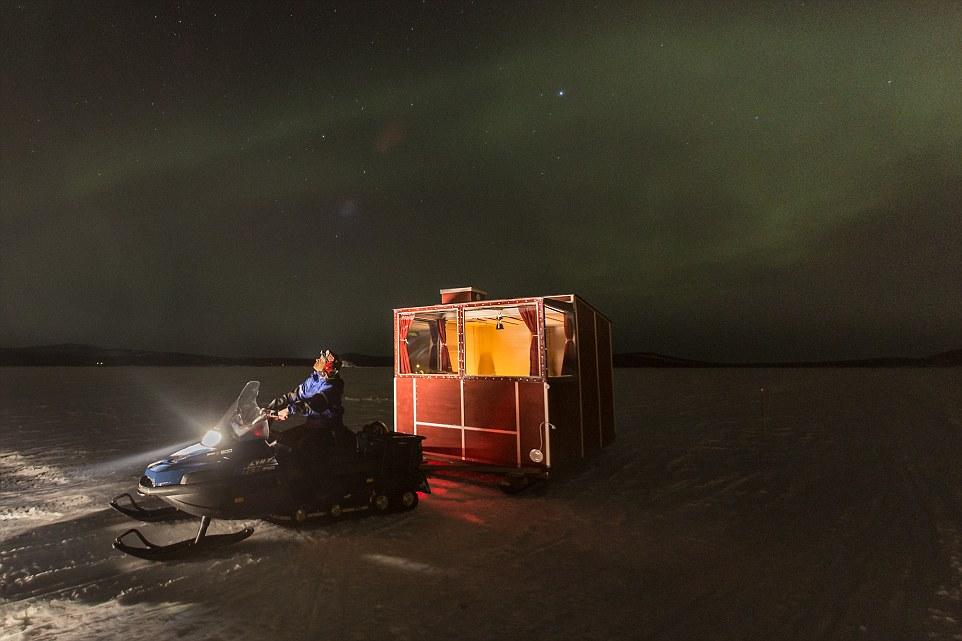 Красный домик Lake Inari с человеком на снегоходе под северным сиянием ночью