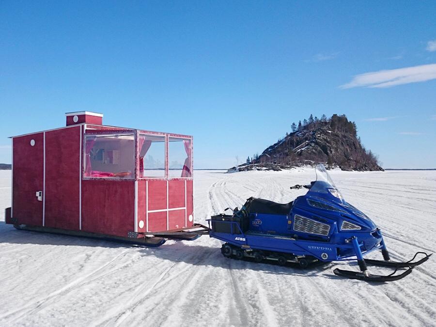 Красный передвижной домик-сани Lake Inari и синий снегоход на льду озера, Финляндия