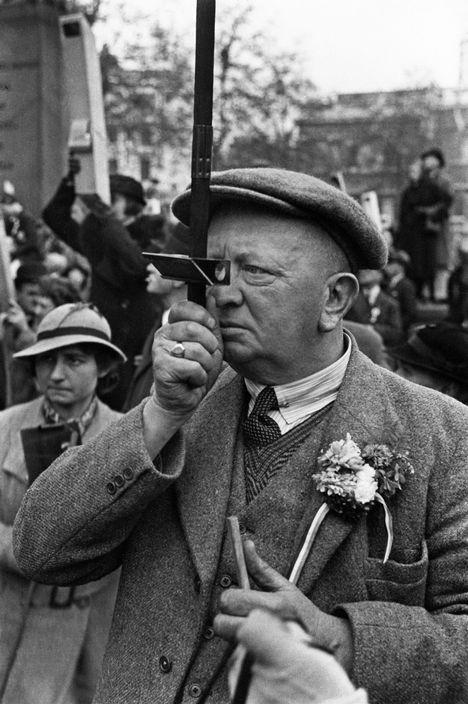 An elderly man in a cap looks through a periscope above the crowd at a demonstration