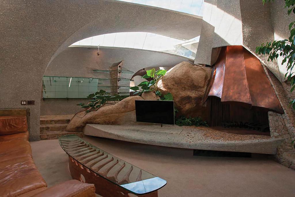 A concrete living room with ribbed vaults, a leather sofa and a boulder on a raised platform