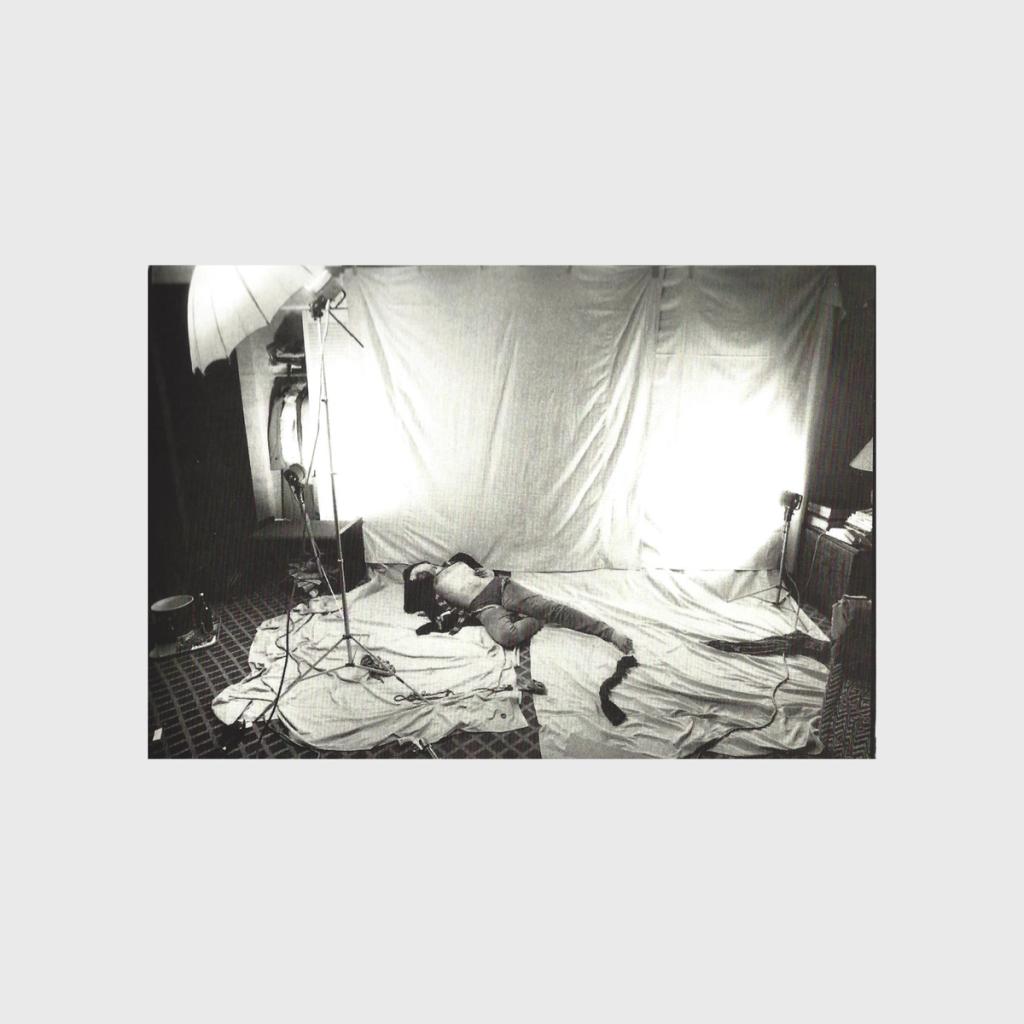 A black-and-white shot of an improvised photo studio backstage, with a person lying against a backdrop
