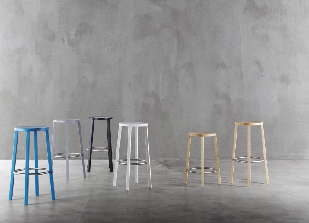 A row of minimalist bar stools in various colours against a concrete wall