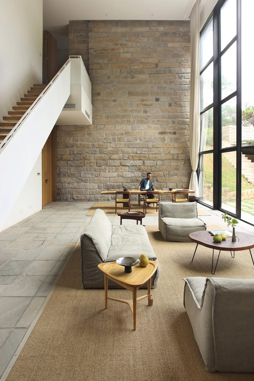 A double-height living room with a stone wall, plush sofas and panoramic glazing