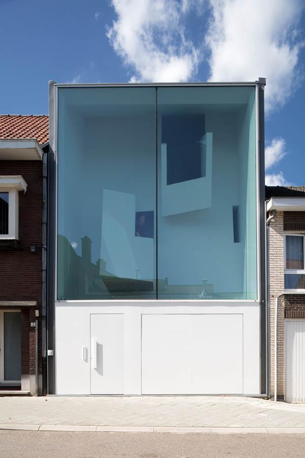 Фронтальный дневной вид узкого стеклянного фасада дома Narrow House с белыми дверями у основания