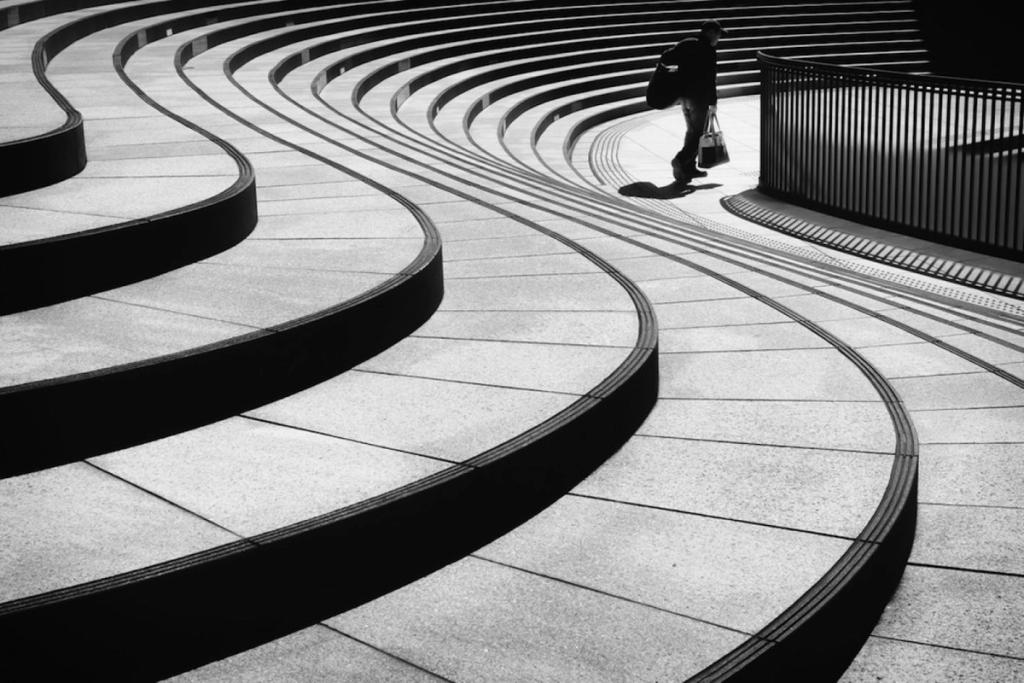 A person descends the curving stone steps of an urban amphitheatre, seen from above