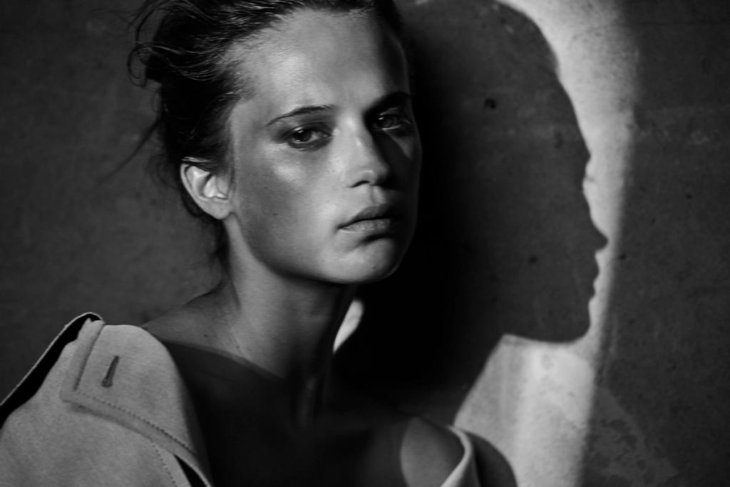 Black-and-white portrait of a woman by a wall, her own shadow beside her