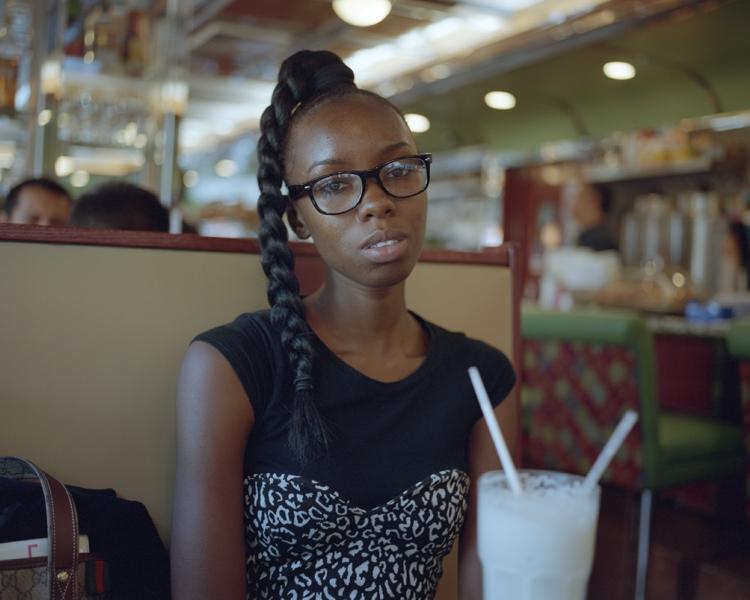 Portrait of a young woman in glasses with a plait, sitting at a café table beside a milkshake