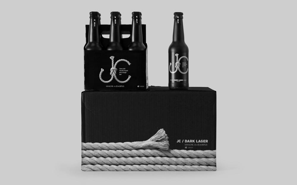 Упаковка из шести бутылок JC Dark Lager на коробке с верёвочным узором