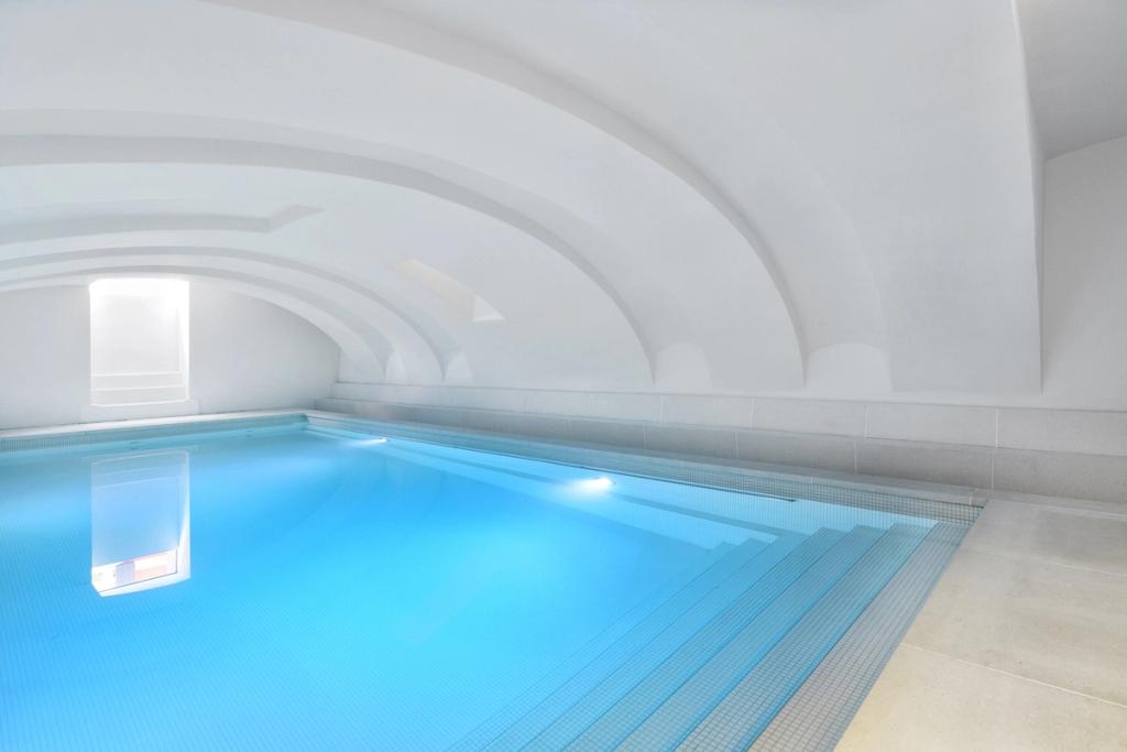 Белый сводчатый бассейн Hotel Zenden с подсветкой и отражением окна в воде