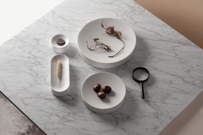 White marble trays and containers with dried flowers and chestnuts on a marble tabletop, designed by Maxim Maximov