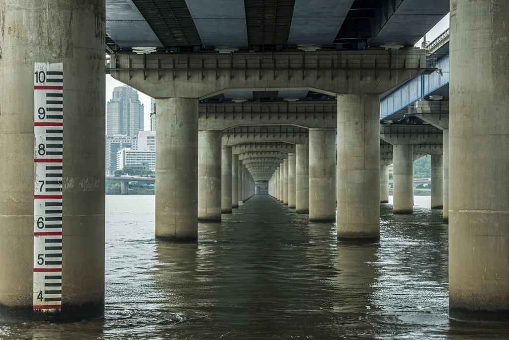 Ряд массивных бетонных колонн моста в воде, шкала уровня воды на ближней опоре